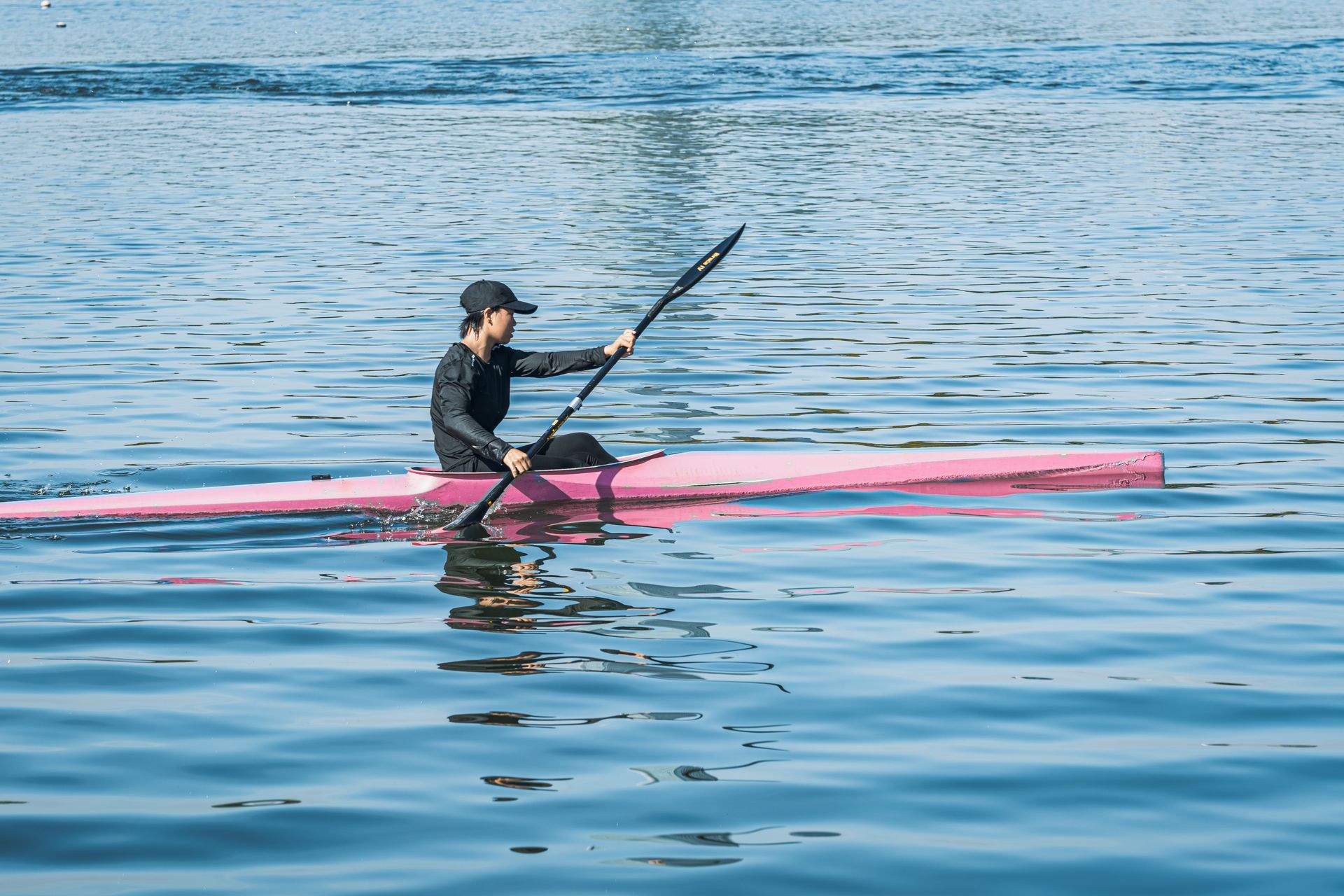 Person kayaking on bright blue water in a pink kayak